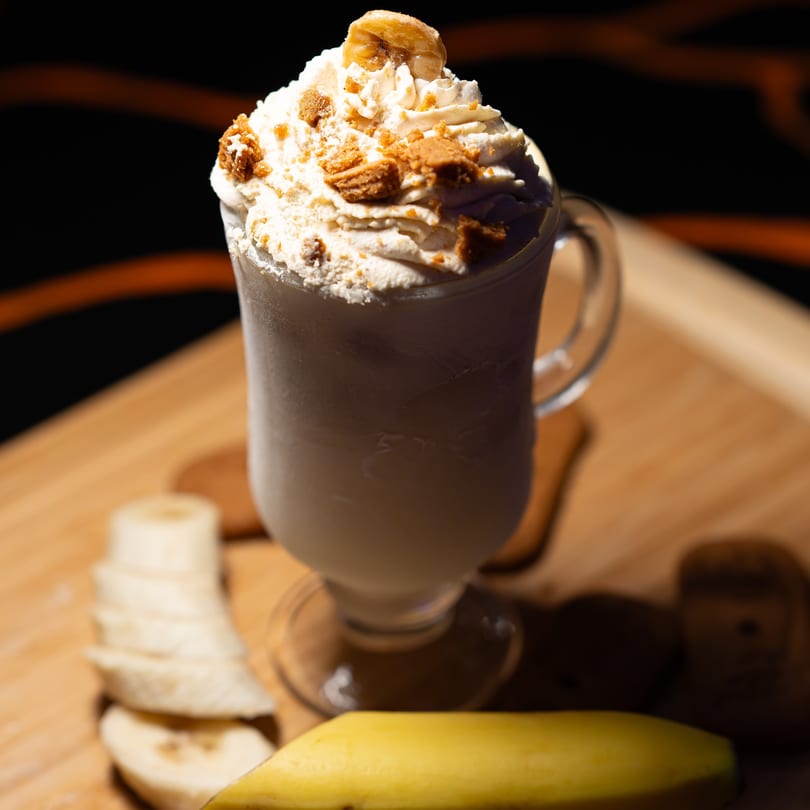 Vegan banana milkshake with whipped cream, cookie crumbles, and a caramelized banana slice.
