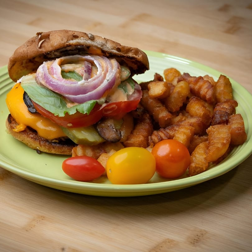 A vegan burger with cheese, lettuce, tomato, onion, and sauce, served with waffle fries and cherry tomatoes.