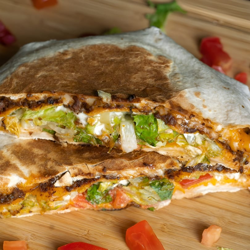 A vegan quesadilla from Plant Based Zo, cut in half, revealing lettuce, tomatoes, and cheese.
